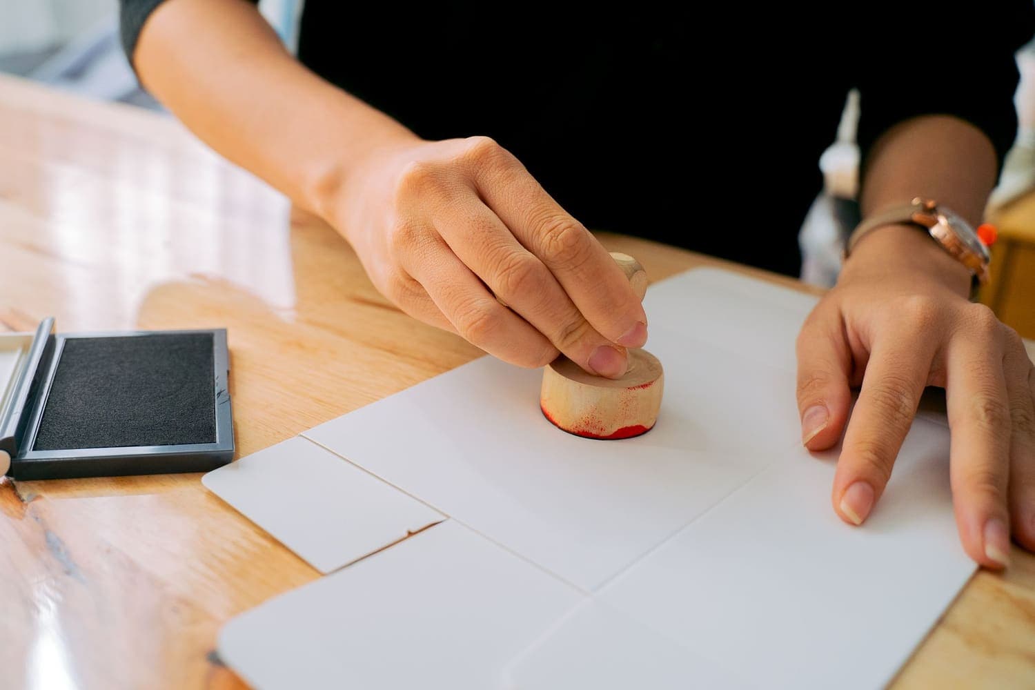A hand pressing an ink stamp onto a paper document on a wooden desk
