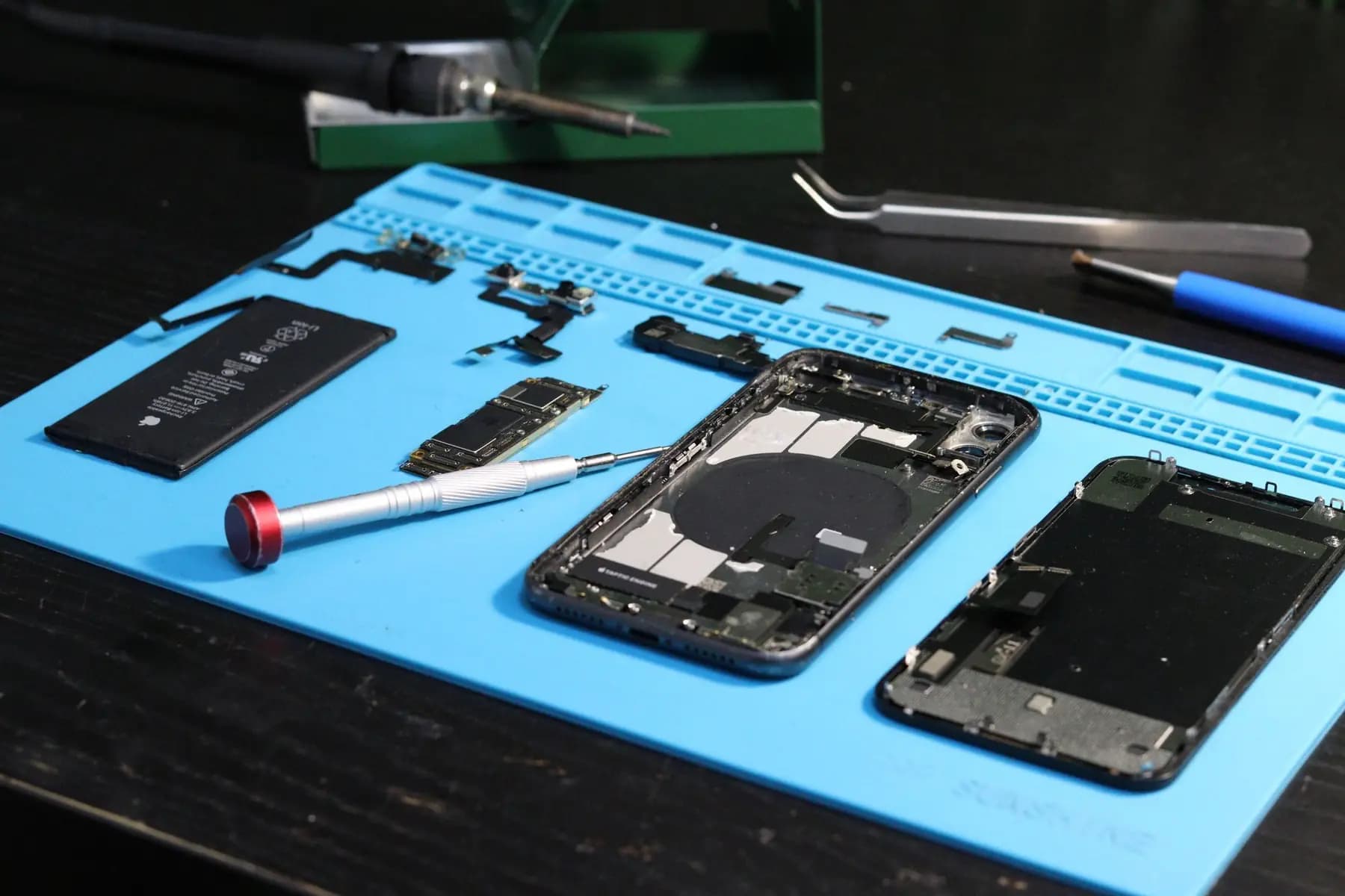 A smartphone taken apart on a repair mat, with its battery, logic board and screen separated