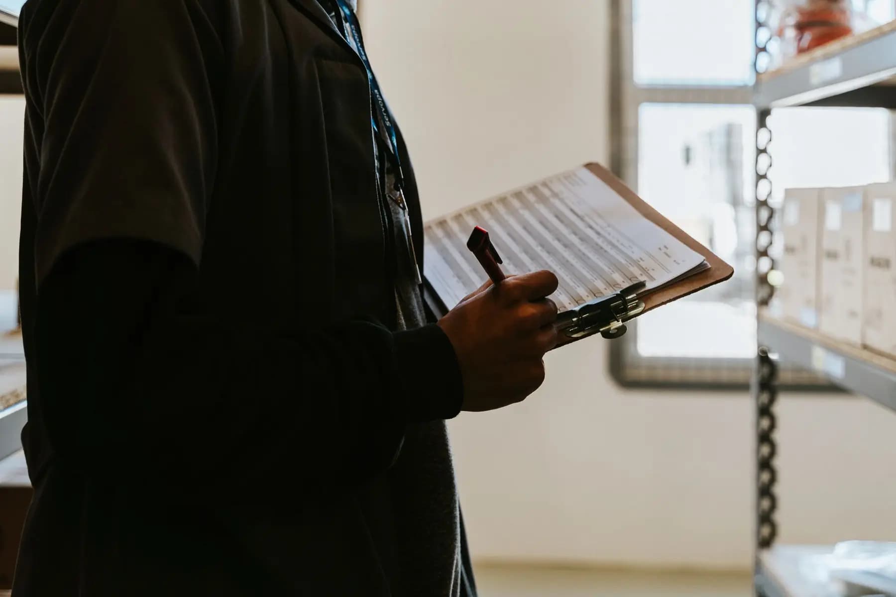 A person filling in a checklist on a clipboard in a storeroom