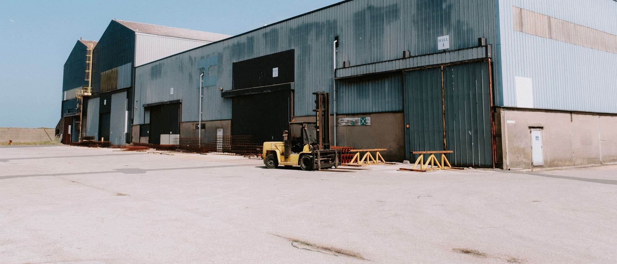 A yellow forklift parked outside the loading doors of a large metal-clad warehouse